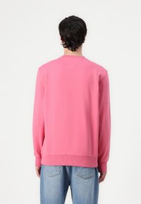 Rosa hettegenser med rund hals, teksturert stoff og ribbestrikkede mansjetter. Kombinert med lyseblå jeans, sett fra baksiden.