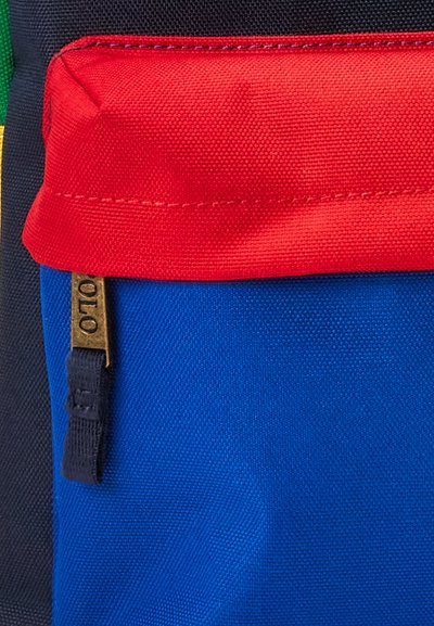 Bolsa textil multicolor con paneles rojos, azules y verdes. Tela texturizada con cierre de cremallera y un acento de hardware en tono dorado.