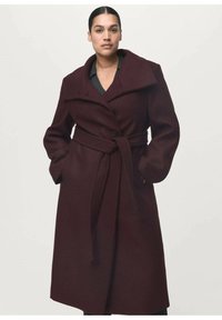 Manteau en laine bourgogne avec grands revers, taille cintrée et poches avant. Le manteau présente une silhouette structurée et une texture lisse.