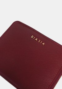 Portafoglio in pelle bordeaux con superficie testurizzata, logo "BIASIA" in rilievo dorato e chiusura a zip. Presenta angoli arrotondati e un bordo liscio.