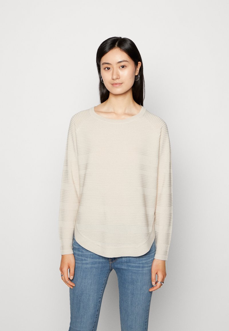 Pull en tricot beige avec un motif rayé texturé, encolure ronde et ourlet arrondi. Assorti à un jeans bleu ajusté.