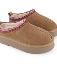 Zapatos tipo slip-on de ante marrón con suela de goma beige, costuras decorativas en rojo y blanco en la parte superior, y un suave forro interior.