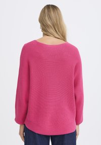 Rózsaszín kötött pulóver laza szabással és széles ujjakkal, mintás textúrával és lekerekített, mély hátkivágással.