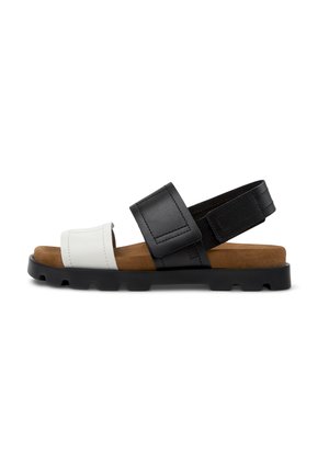 Black and white sandal with a flat sole, adjustable straps, and a brown suede insole; features a smooth texture and minimalistic design.
