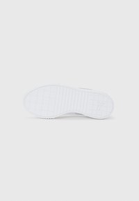 Sole of white sneaker with grid and horizontal line tread pattern, featuring a Puma logo near the heel.
