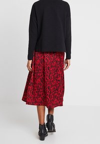Haut noir à manches longues associé à une jupe midi rouge et noire à motif. La tenue présente une coupe décontractée avec un tissu doux et des bottines.