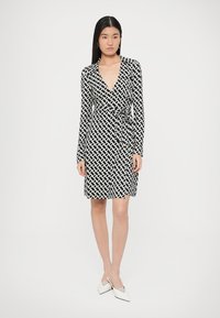 Črno-bela obleka z ovijalnim dizajnom, dolgimi rokavi in geometričnim vzorcem. Tkanina je gladka z oprijeto silhueto.