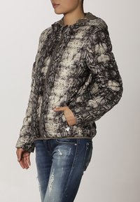 Vadderad jacka i ett beige och svart ormskal-mönster, med dragkedjestängning, huva och sidofickor. Texturerat tyg med glänsande accenter.