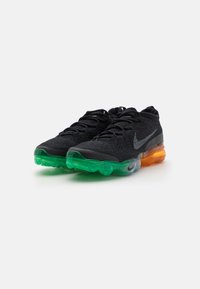 Nike sneakers featuring a black textile upper, green and orange air cushioning sole, with a reflective silver logo and textured design.