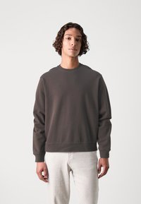 Mørkegrå sweatshirt med rund halsudskæring samt ribbede manchetter og kant. Enkelt design med en blød tekstur, parret med lyse bukser.