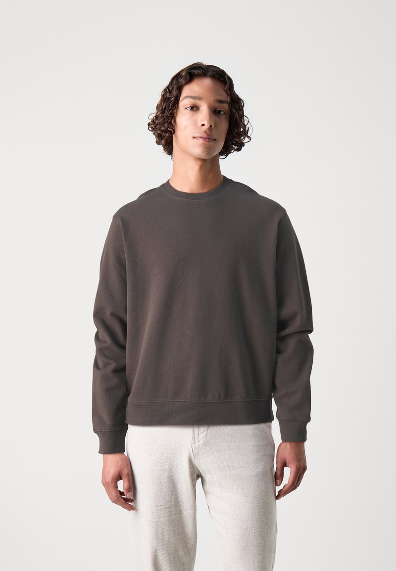 Mørkegrå sweatshirt med rund halsudskæring samt ribbede manchetter og kant. Enkelt design med en blød tekstur, parret med lyse bukser.