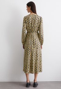 Lang�ärmliges Midi-Kleid mit einem gelben, schwarzen und braunen kreisförmigen Muster. Es hat eine taillierte Taille und einen fließenden Rock. Hergestellt aus einem leichten Stoff.