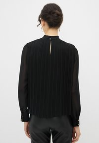 Blusa nera plissettata con maniche lunghe, polsini con bottoni e apertura a chiave sul retro. Realizzata in tessuto leggero e strutturato.