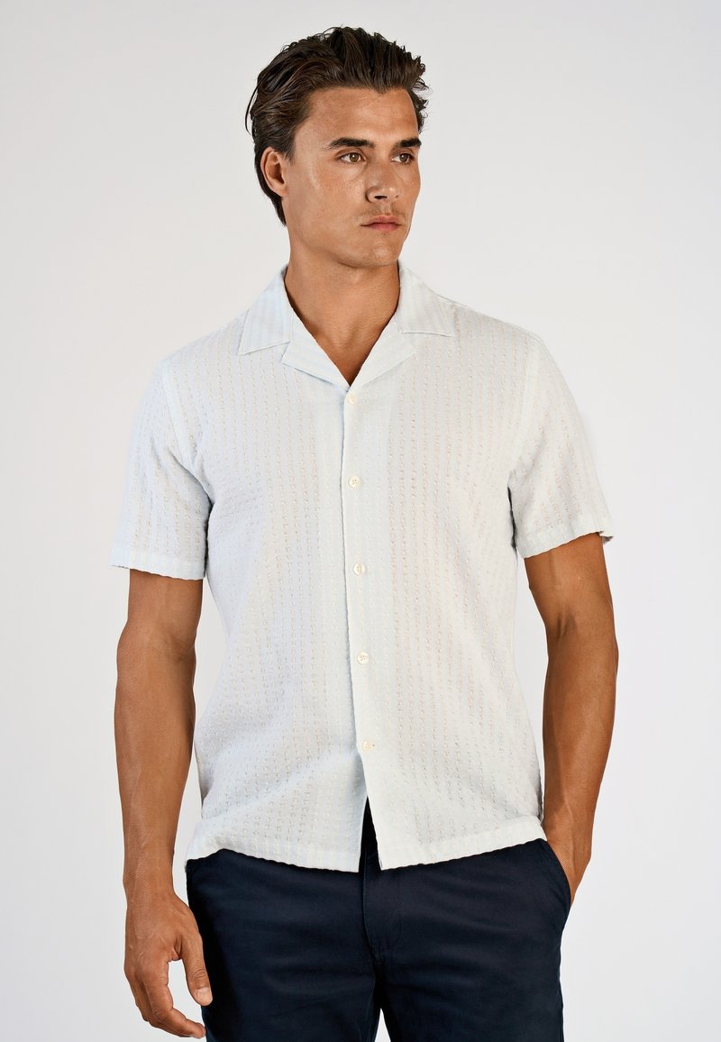 Jasnoniebieska koszula z krótkim rękawem o fakturowanym wzorze, z zapięciem na guziki i kołnierzem typu spread, zestawiona z ciemnymi spodniami.