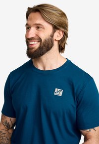 Mörkblå bomullströja med rund halsringning och korta ärmar. Inkluderar en liten, fyrkantig logotyp-patch på vänster bröstområde.