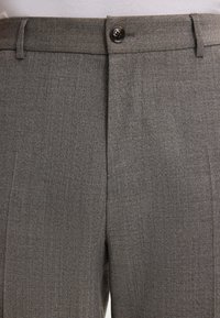 Pantaloni grigi su misura con una finitura testurizzata. Presentano un frontale piatto, chiusura a bottone e cuciture rinforzate per una maggiore durata.
