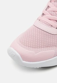 Chaussure de sport rose clair avec une tige en mesh, languette rembourrée et semelle en caoutchouc blanche. Bout arrondi et accents texturés près de l'avant.