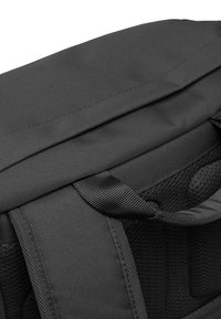 Černý látkový batoh s texturovaným povrchem, vybavený horní klopou, nosnými úchyty a síťovanými částmi pro ventilaci.