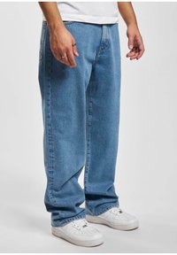 Jeans de mezclilla azul claro con un corte relajado y piernas rectas, que presentan un diseño clásico de cinco bolsillos y detalles de costura sutiles. Usados con zapatillas blancas.