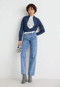 Camicia a maniche lunghe a motivo navy con accento argentato, abbinata a jeans azzurri chiari con dettagli borchiati e stivaletti argento. Borsa nera.