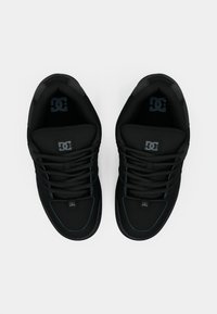 Crne sportske tenisice s teksturiranim gornjim dijelom, podstavljenim ovratnikom i crnim vezicama. Imaju logotip na jeziku i detalje šavova.