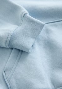 Hele sinine dressipluusi kangas, mis näitab soonikutega mansetti ja sujuvat tekstuuri, nähtavate õmblusdetailidega tugevdatud õmbluste jaoks.