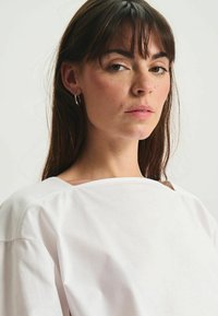 T-shirt blanc oversize avec un large col et des manches courtes, présentant une texture lisse et des détails de couture minimaux.