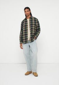 Knapp-up ternet skjorte i grønne, brune og blå nuancer, parret med lyseblå løse jeans og brune sneakers. Glat stofstruktur med en afslappet pasform.