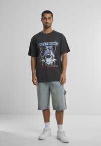 Donkergrijze oversized t-shirt met grafische print van een brullende hond, gecombineerd met lichtblauwe denim shorts en witte sneakers.