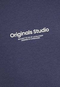 Navyblauer Baumwollstoff mit glatter Textur und bedrucktem weißen Text, der "Originals Studio" und "Brought to you by JACK&JONES" angibt.