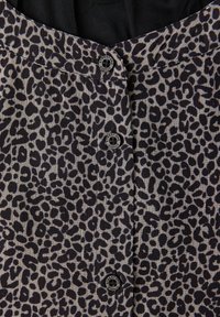 Gros plan sur un tissu gris avec des taches léopard noires irrégulières et trois boutons ronds noirs portant l'inscription "Street One Studio".