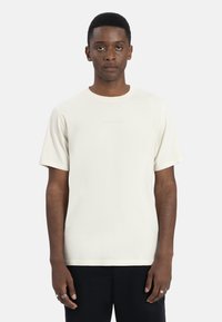 Korte mouwen crème t-shirt van zachte stof met een ronde hals, met subtiele branding in een lichtere tint op de voorkant.