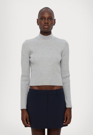 Pull en col roulé gris à côtes, longueur crop, avec des manches longues associé à une jupe bleu marine foncé. Le matériau semble doux et ajusté.