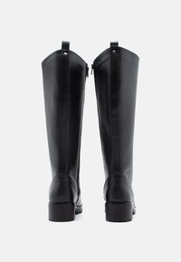 Botas de piel negras hasta la rodilla con una textura suave, puntera redondeada y tacón cuadrado. Presentan una cremallera en la parte posterior y un tirador para facilitar el calzado.