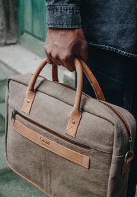 Canvas laptop bag with leather accents, tan handles, and a front zip pocket. Features sturdy stitching and a textured, neutral color.