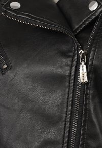 Giacca di pelle nera con hardware argentato. Presenta una zip frontale, colletto con bottone a scatto e una superficie testurizzata con dettagli di cucitura visibili.