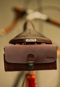 Bruin leren fietsenzadel met een bijpassende bruine leren tas voorzien van een metalen sluiting en een gegraveerd merkelogo. Geïnspireerde textuur, slank ontwerp.