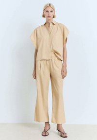 Conjunto de dos piezas en beis con camisa de botones de manga corta y pantalones con cintura elástica; tejido ligero, corte holgado, piernas de pantalón acampanadas.