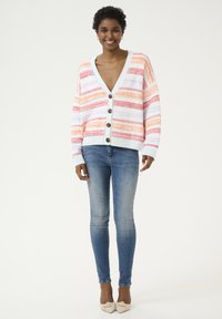 Gilet tricoté avec un décolleté en V profond, des rayures multicolores en orange, rose et blanc, muni de boutons et de poignets à côtes, associé à un jean skinny.
