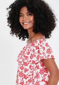 Top off-shoulder in un tessuto bianco con motivi floreali rossi. Presenta un colletto arricciato e maniche corte, design leggero e fluido.