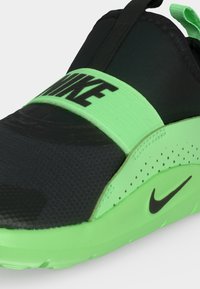 Μαύρο και νέον πράσινο sneaker slip-on της Nike με ελαστικό λουράκι στην κορυφή και μαύρο λογότυπο Nike στο πλευρό της σόλας σε νέον πράσινο χρώμα.