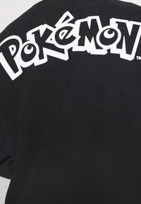 Felpa nera con un grande logo bianco "Pokémon" facilmente visibile sul retro, con caratteri in grassetto e bordi arrotondati.