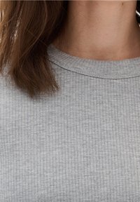 Grå ribbad topp med rundad halsringning. Tyget har en mjuk textur med jämnt fördelade vertikala linjer och en avslappnad passform.