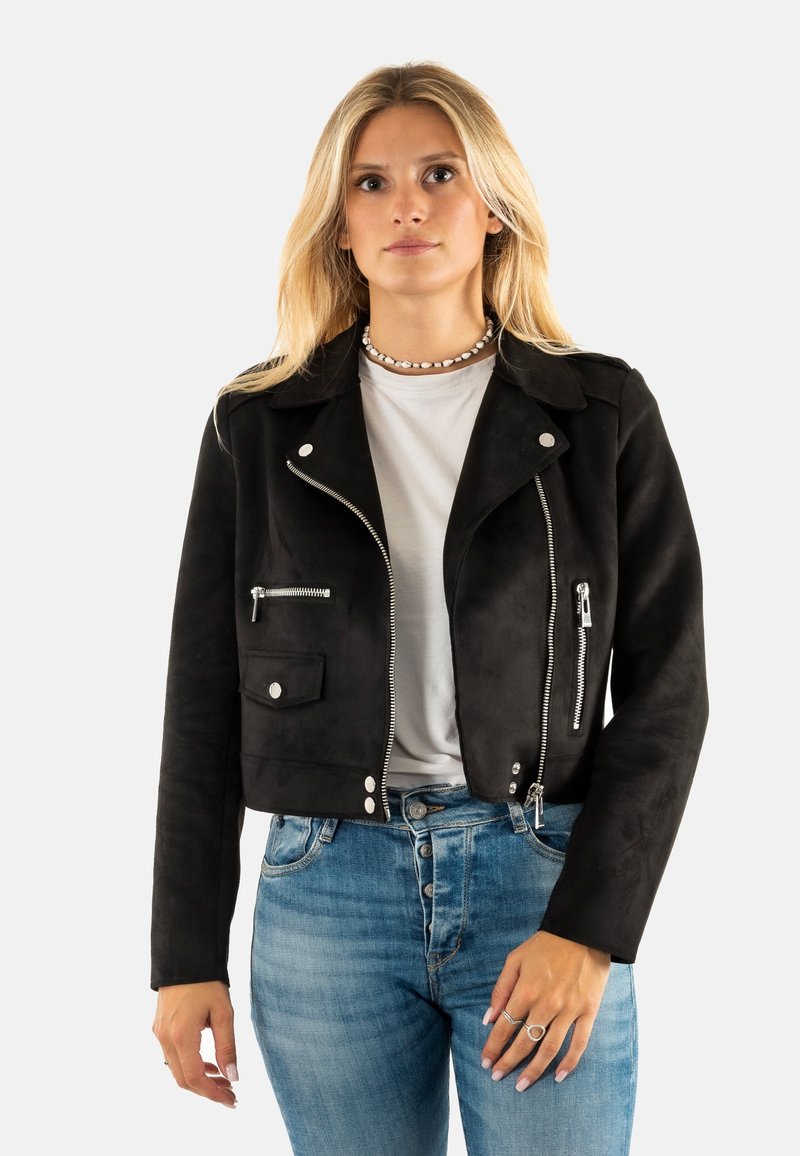 Chaqueta corta de ante negro con cierre frontal, herrajes plateados, bolsillos laterales y un diseño clásico de cuello. Combinada con jeans azules.