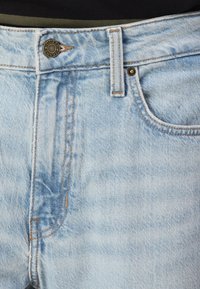 Jeans de denim de color azul claro con cremallera, cierre de botón y costuras naranjas. Incluyen un bolsillo frontal y un lazo para cinturón en la cintura.