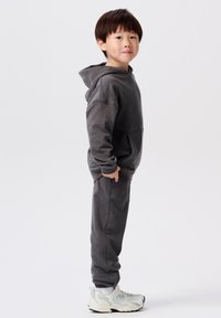 Grijze hoodie met een kangoeroezak, gecombineerd met bijpassende trainingsbroeken. Gecombineerd met witte sneakers met lichtgroene accenten.