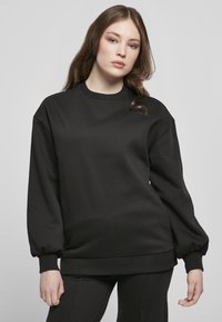 Felpa nera con collo rotondo, spalle basse e maniche a palloncino. Realizzata in tessuto spesso e liscio, con polsini e orlo a coste.
