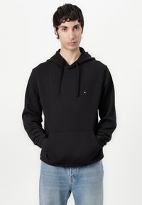 Zwarte pullover hoodie met een voorzak, trekkoord en klein embleem. Glad textiel, normale pasvorm, gecombineerd met lichtblauwe spijkerbroek.