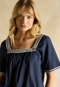 Bluză bleumarin cu decolteu pătrat, prezentând un corp strâns și accente cu dungi albe pe marginea decolteului și mâneci. Textură netedă.