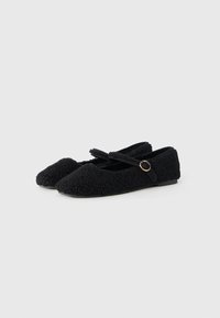 Bailarinas negras hechas de un tejido texturizado con un aspecto suave y peludo. Cuenta con una suela plana y una correa entrecruzada con un pequeño acento dorado.